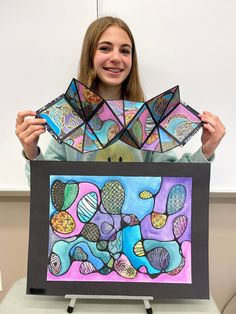 a girl holding up two pieces of art that are made out of stained glass and paper