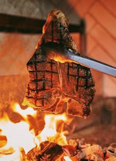 a steak being cooked on the grill with tongs over it's head and flames in the background