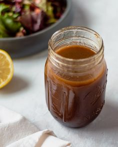 a mason jar filled with brown liquid next to a bowl of salad and lemon wedges