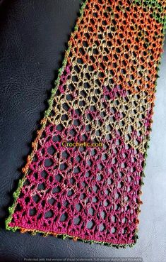 the crocheted table runner is made with multicolored yarn and sits on a black surface