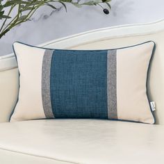 a blue and white pillow sitting on top of a couch next to a potted plant