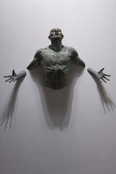 a sculpture of a man's torso and hands in the air, against a white wall