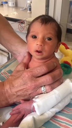 a baby is being held by an adult in a hospital bed with his arm around the infant's head