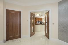 an empty hallway leading to a kitchen and living room with wood doors on both sides