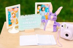 a table topped with two pictures and a stuffed animal next to a camera on top of a wooden table