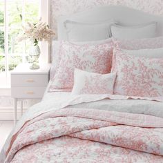 a bed with pink and white comforters on top of it in front of a window