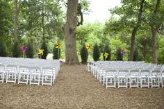 rows of white folding chairs with colorful pinwheels on them in front of a tree