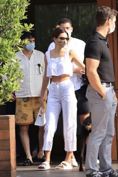 a woman in white pants and top standing next to two men wearing facemasks