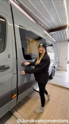 a woman standing next to a van in a garage with her hands on the door