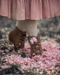 a close up of a person's feet with pink flowers on the ground in front of her