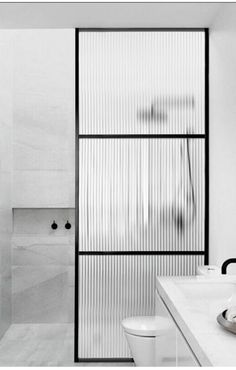 black and white photograph of a bathroom with two sinks, toilet and shower stall in the background