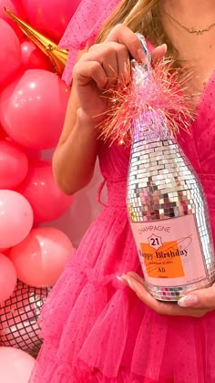 a woman in a pink dress holding a bottle of booze next to balloons and streamers