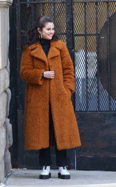 a woman in a brown coat is standing outside