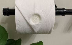 a roll of toilet paper sitting on top of a black towel rack next to a green plant