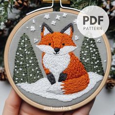 a hand embroidered fox sitting in the snow with pine trees on it's back