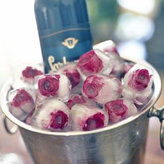 a metal bucket filled with ice and roses next to a bottle of wine on top of a wooden table