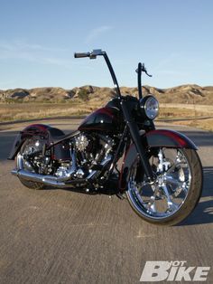 a black and red motorcycle is parked on the side of the road with hills in the background