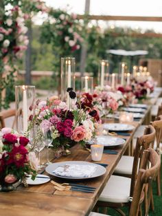 a long wooden table topped with lots of plates and vases filled with pink flowers