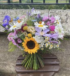 a bouquet of flowers sitting on top of a wooden bench next to a stone wall