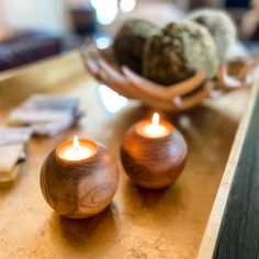 two tea lights sitting on top of a wooden table next to a bowl filled with rocks