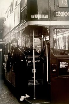 a black and white photo of a man standing next to a double - decker bus