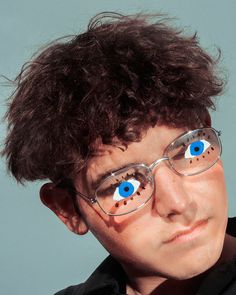 a young man wearing glasses with blue eyeballs on his face and hair in the wind