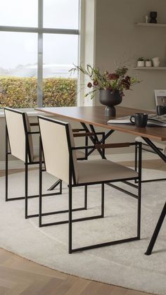 a dining room table with four chairs and a laptop on top of it, in front of a large window