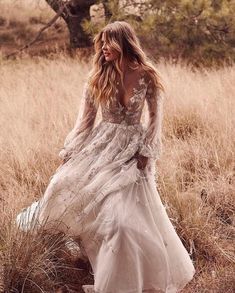 a woman in a long white dress is walking through the grass