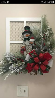 a christmas wreath with snowmen and evergreens hanging on the wall next to a light switch