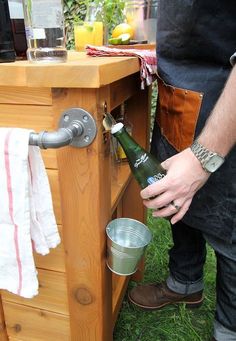 a man holding a beer bottle next to a wooden table with an ice bucket on it