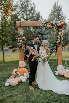 a bride and groom standing in front of an arch decorated with pumpkins and flowers