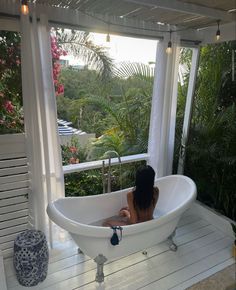 a woman sitting in a bathtub on top of a wooden floor next to a window