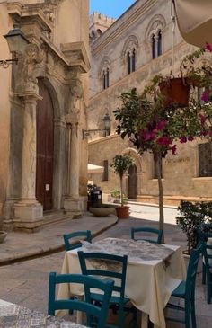 tables and chairs are set outside in front of an old building with flowers on it