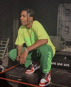 a man sitting on top of a stage with his hands in his pockets and wearing green pants