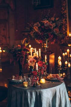 a dining table with candles and flowers in vases on the top, surrounded by other place settings