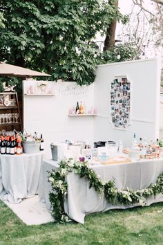 a table covered with bottles and glasses on top of a lush green field next to a tree