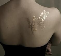 the back of a woman's shoulder with gold tattoos on her upper arm and chest