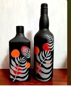 two black bottles with orange and white designs on them sitting on a wooden table next to each other