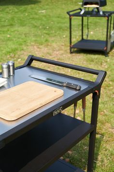 a table with a cutting board on it in the middle of a grassy area next to some chairs