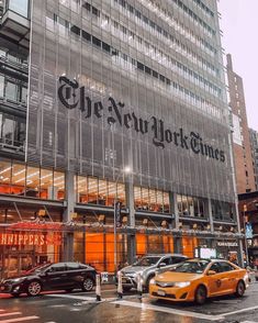 the new york times building is lit up at night with cars parked on the street