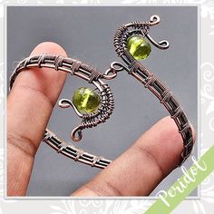 a hand holding a piece of metal with green stones on it's sides and an ornate design around the edges