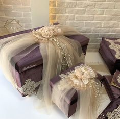 purple and white gift boxes with lace on them sitting next to each other in front of a brick wall