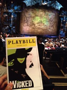 a person holding up a playbill magazine in front of an audience at a theater