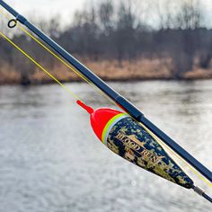 a fishing rod with a red and yellow handle on the side of a body of water