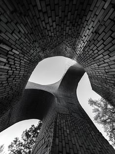 looking up at the top of a tall brick structure with trees in the foreground