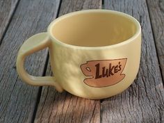 a yellow coffee cup with the words luke's on it sitting on a wooden table