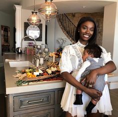 a woman holding a baby in her arms while standing next to a kitchen counter top