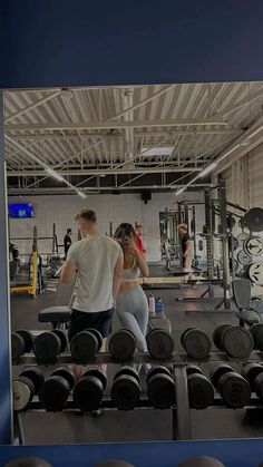 a man and woman walking through a gym with dumbbells on the floor in front of them