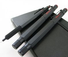 three pens sitting on top of a black notebook next to an empty notepad and pen