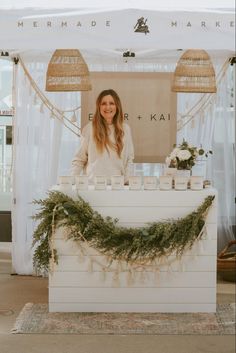 a woman standing behind a white counter with candles and flowers on it in front of a tent